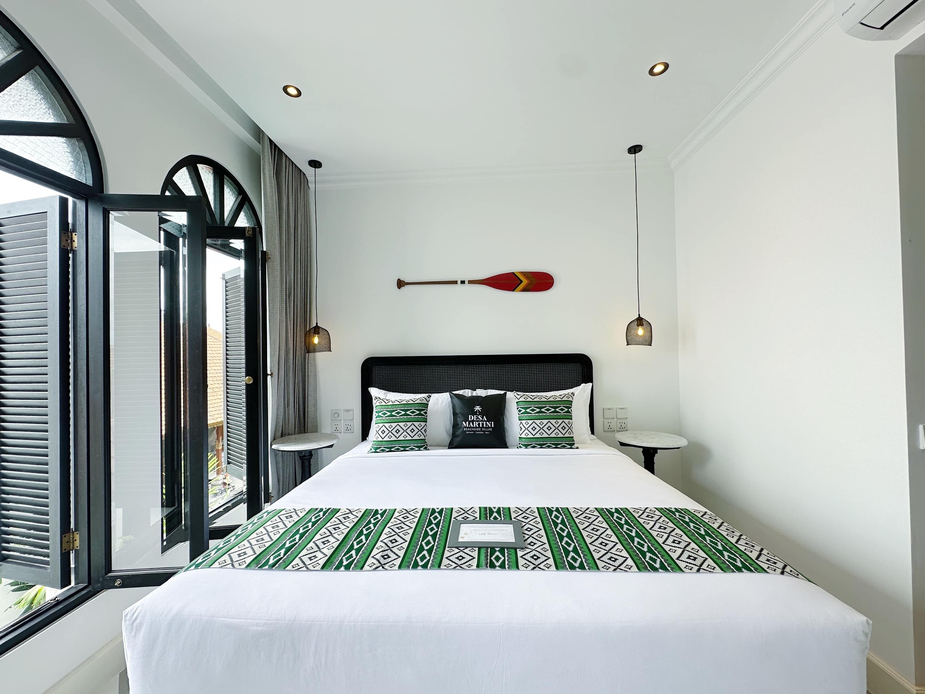 A hotel room with a bed, a red paddle on the wall, and two pendant lights.