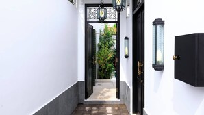 Un corridoio stretto con una porta nera e un muro bianco. Sopra la porta, due lampade nere in stile lanterna.