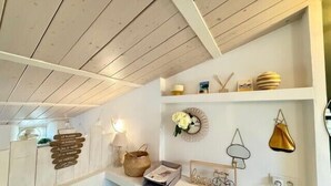 Ein gemütliches Zimmer mit Holzbalkendecke, weißen Wänden und einem Regal mit Dekoration.