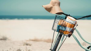 Ein Fahrrad mit Korb, der eine Flasche und eine Dose enthält, und einem Sonnenschutzhut am Lenker.
