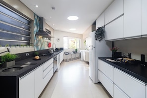 A modern kitchen with a central island, built-in appliances, and a view to the outside. - Casa a 450m Parque Ipiranga (São Paulo)