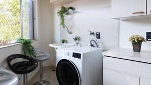 A modern kitchen with a built-in washing machine, a sink, and bar stools. - Casa a 450m Parque Ipiranga (São Paulo)