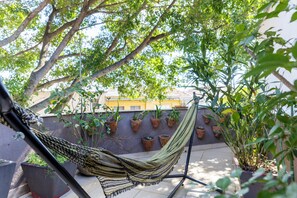 Un hamac sur un balcon, avec des plantes en pot et un immeuble en arrière-plan.