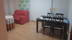 A room with a red sofa, a dining table with chairs, a small round table with a patterned tablecloth, and a curtain with a green and white checkered pattern. - Apartment 'Piso Centroolula' with Balcony and Air Conditioning (Olula del Río)