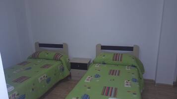 Een tweepersoonskamer met twee eenpersoonsbedden, elk met een groene spreidek en een houten hoofdbord. Er staat een klein nachtkastje met een lamp en een doos erop.