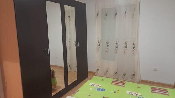 A room with a wardrobe, a bed with a green bedspread, and a window with a sheer curtain. - Apartment 'Piso Centroolula' with Balcony and Air Conditioning (Olula del Río)