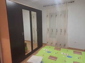 A room with a wardrobe, a bed with a green bedspread, and a window with a sheer curtain.