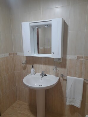 Un baño con lavamanos pedestal, espejo encima y toalla colgada en un perchero.