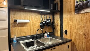 Une cuisine dotée d’un évier en acier inoxydable, d’un plan de travail noir, de placards en bois, de casseroles suspendues et d’un porte-rouleau en papier.