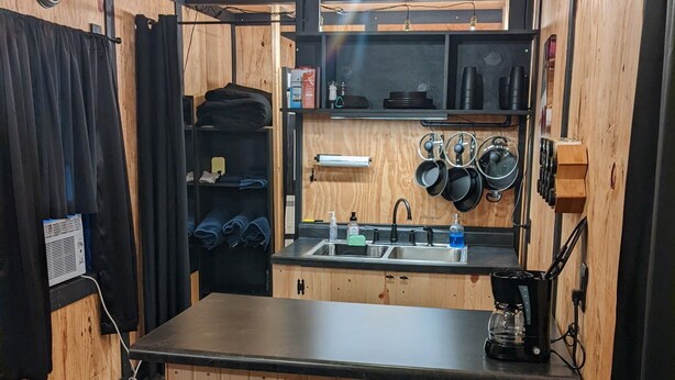 Une cuisine compacte dotée d’un plan de travail en bois, de deux tabourets, d’une machine à café et de divers ustensiles de cuisine.