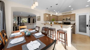 A dining area with a wooden table set for four, a kitchen with wooden cabinets, and a sign that reads 'OUR HAPPY PLACE'. - Surfer`s Paradise! Walk to Beach, Parking (San Diego)