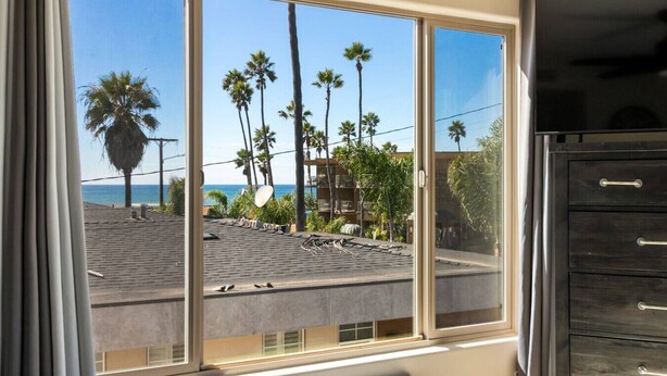 A room with a large window overlooking a rooftop with palm trees and a building in the background. - Surfer`s Paradise! Walk to Beach, Parking (San Diego)