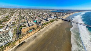 An aerial view of a coastal city with a beach, a pier, and a mix of residential and commercial buildings. - Surfer`s Paradise! Walk to Beach, Parking (San Diego)