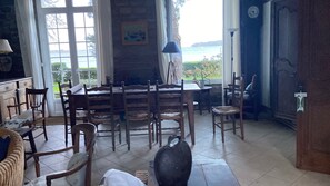 A dining area with a table and chairs, a fireplace, and a view of the sea through large windows.
