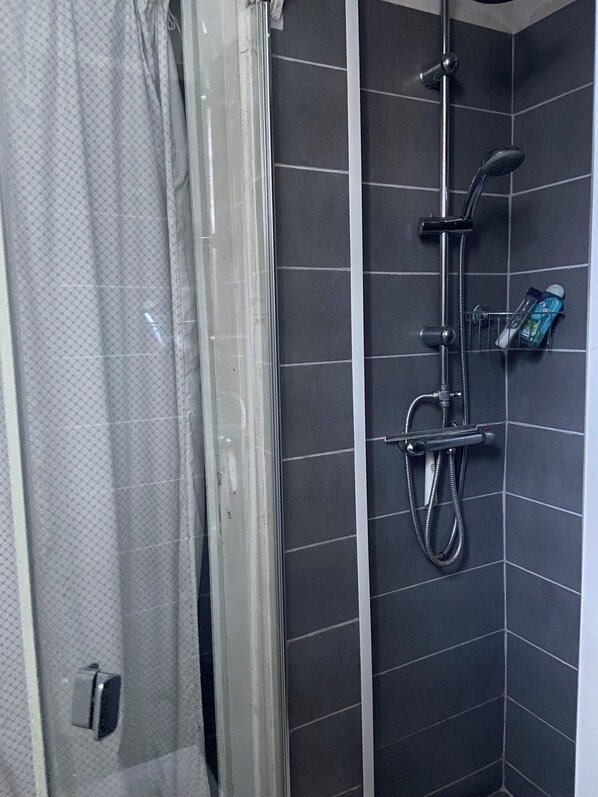 A shower area with a glass door, a handheld showerhead, a wall-mounted faucet, and a soap dispenser.