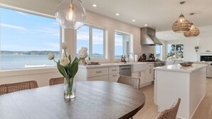 A modern kitchen with large windows, a dining area with a round table, and a view of the sea. - Pearl House Beach Retreat (Poulsbo)