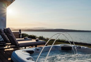 Ein Whirlpool mit Unterwasserdüsen, Liegestühlen und Blick auf einen See mit Bergen im Hintergrund.