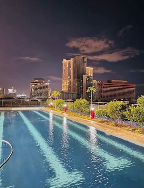 A swimming pool with a city skyline in the background. - Carnivale Inn Staycations (Manila)
