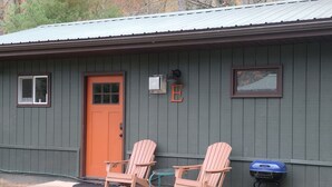 Un bâtiment à l’extérieur gris, avec une porte rouge et deux fauteuils Adirondack placés à l’extérieur.