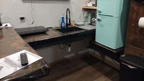 Une cuisine de taille réduite, équipée d’un évier, d’un réfrigérateur de couleur turquoise et d’une fenêtre située au-dessus du plan de travail.