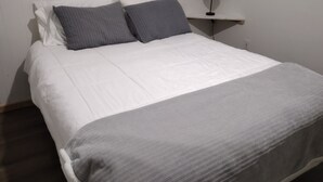 Un lit bien fait, avec une literie blanche et grise, une table de chevet avec une lampe et un mur blanc.