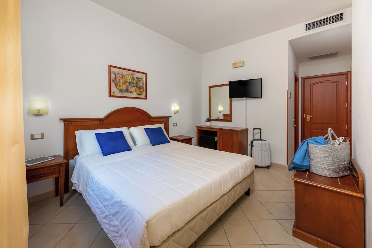 A hotel room with a large bed, a desk, a TV, and a wardrobe.