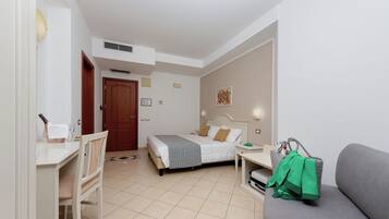 Une chambre d’hôtel avec un lit, un bureau, une chaise, un canapé et une petite table sur laquelle se trouve un sac vert.