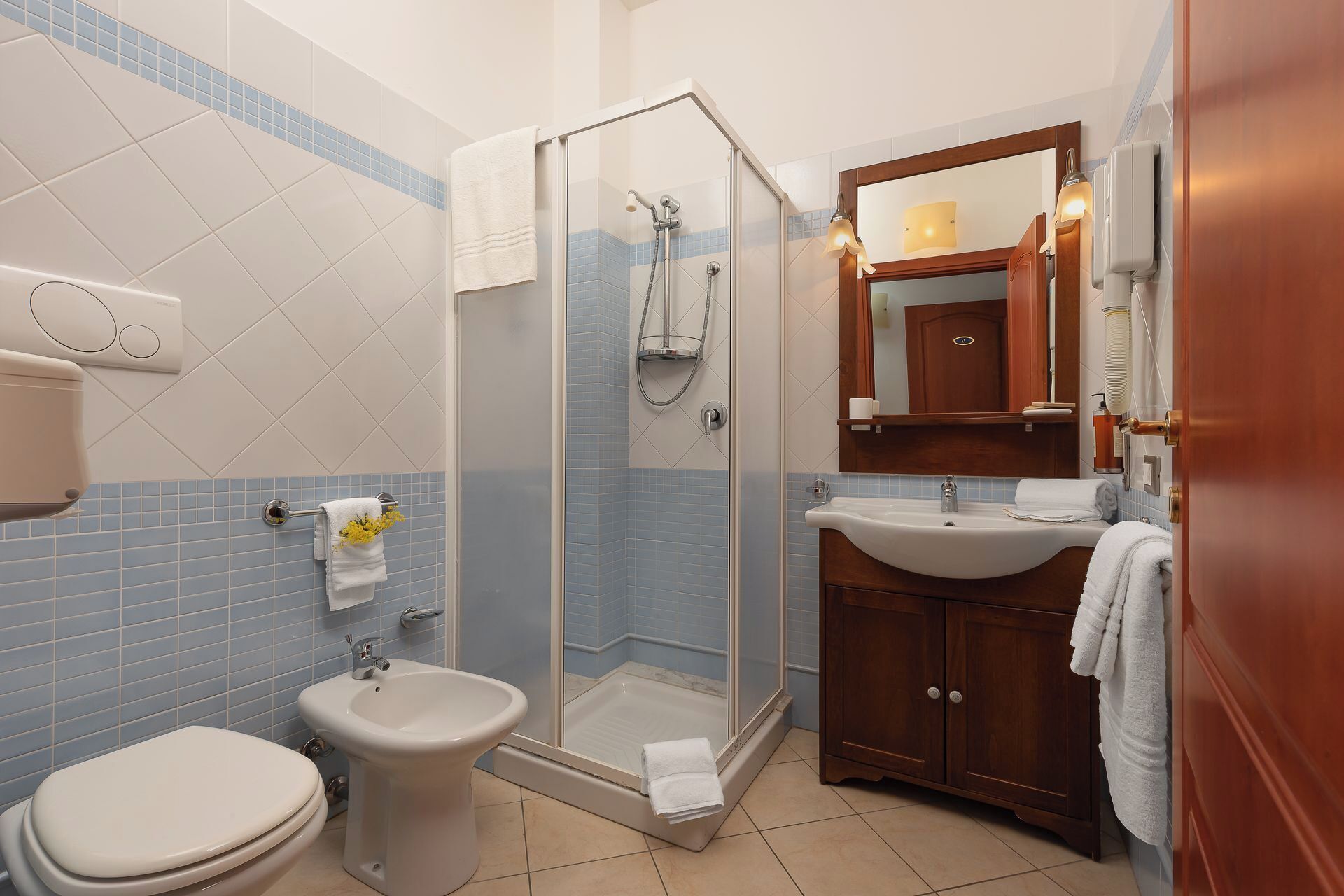 Een badkamer met een douche met glazen wand, een bidet, een wastafel en een houten kastje.