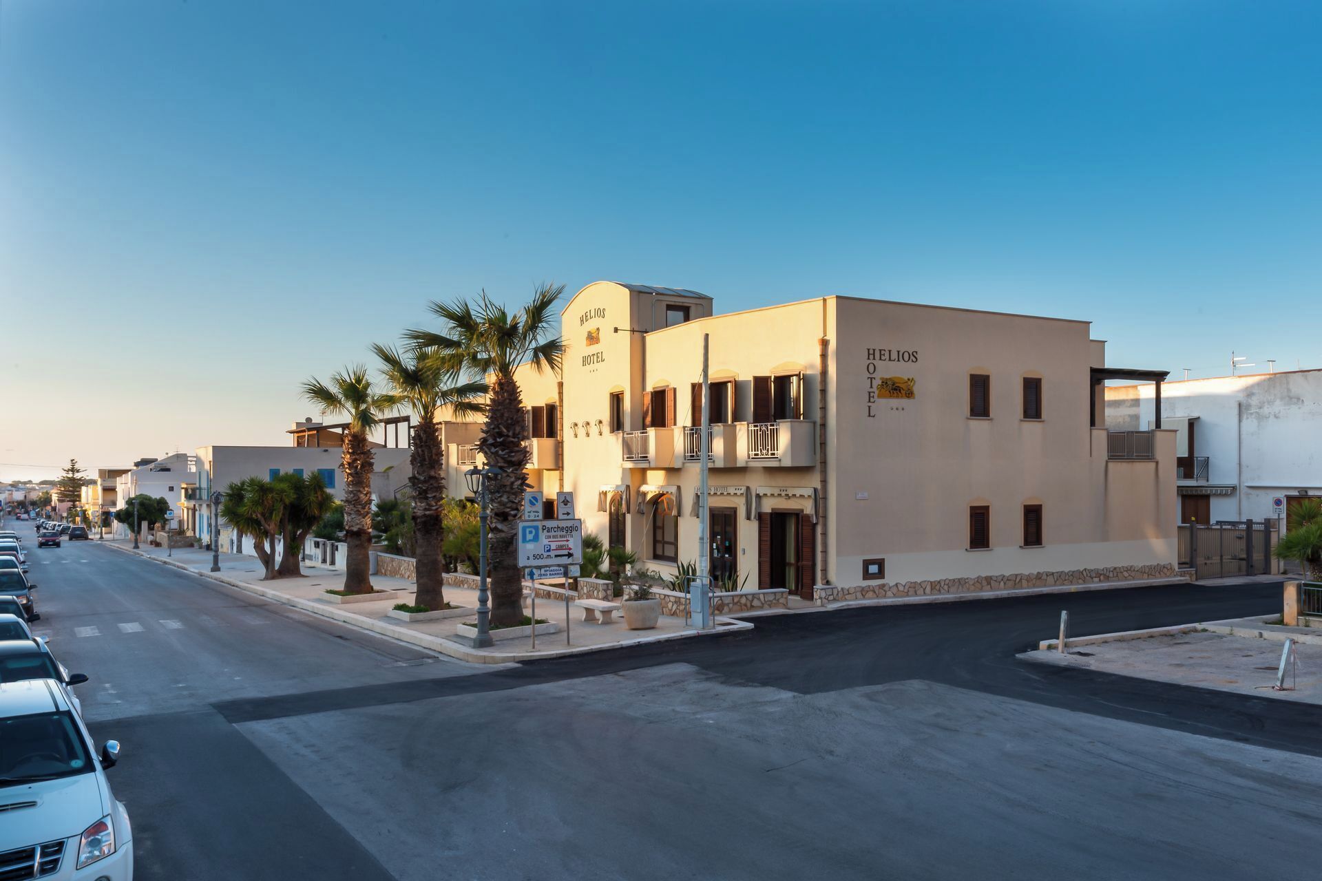 A hotel named 'HIELIOS' with a modern design, located on a street with parked cars and palm trees.