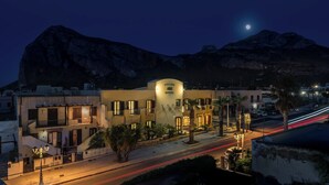 A hotel with a curved facade, multiple balconies, and a view of mountains in the background. - Helios Hotel (San Vito Lo Capo)