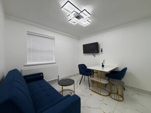 Un soggiorno moderno con un divano blu, un tavolino rotondo e una TV a parete.