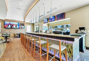 Un espace bar doté d’un long comptoir, de plusieurs téléviseurs et d’un coin salon avec des tabourets.