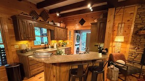 Una cucina rustica con mobili in legno, una grande isola con sgabelli da bar, un muro in pietra e vista all'esterno attraverso le finestre.