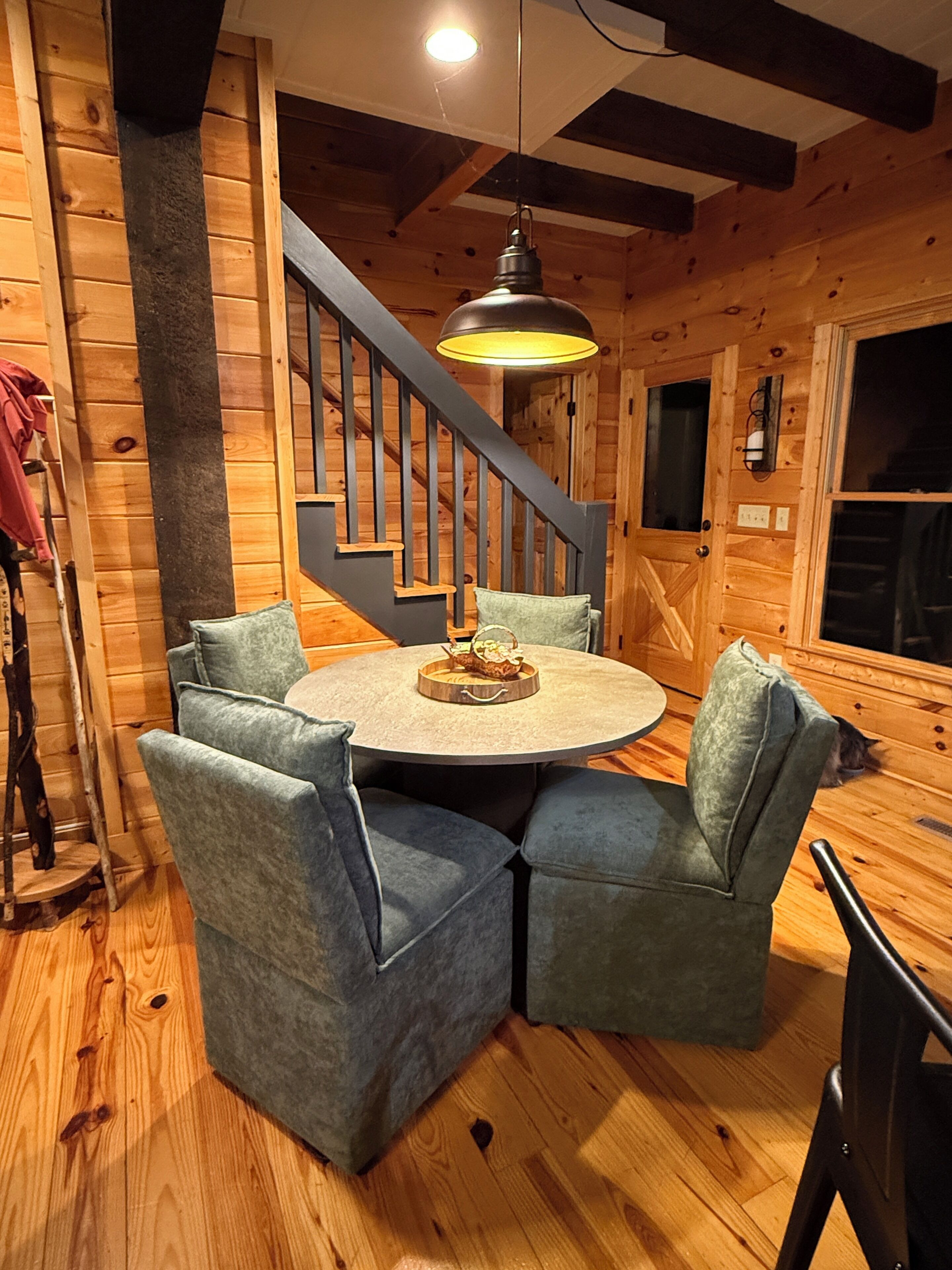 A wooden interior with a round table and four blue chairs, a staircase, and a hanging light fixture.