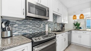 A modern kitchen with white cabinets, a stainless steel microwave, a gas stove, and a tiled backsplash. - Healthier Beachfront Stay - Short Walk to Flagler (New Smyrna Beach)