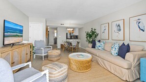 A living room with a television, sofa, chairs, and a dining area with a table and chairs. - Healthier Beachfront Stay - Short Walk to Flagler (New Smyrna Beach)