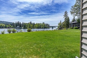 A grassy lawn with a view of a lake, trees, and a bridge. - Cozy Bigfork Retreat Near Flathead Lake (Bigfork)