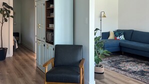 Uma sala de estar moderna com piso de madeira, uma poltrona escura, um armário azul claro, um sofá azul e um tapete estampado.