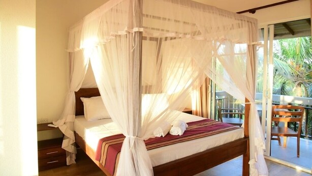 A four-poster bed with a canopy, wooden flooring, a small bedside table, and a view of a palm tree through a glass door. - DADY`S Place `63`- Sunset Villa - 1 Floor - Beach in 2 Min (Hikkaduwa)