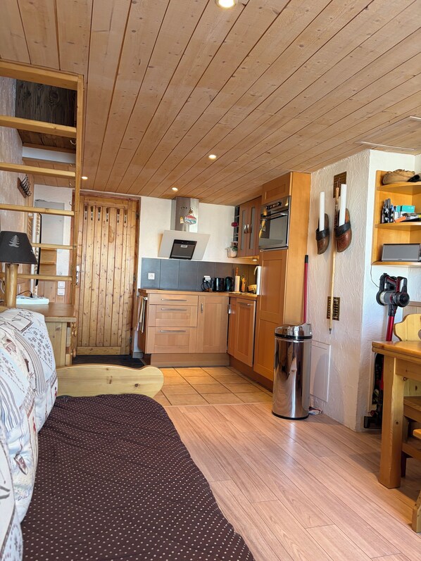 A cozy room with a bed, a desk, a laptop, and a kitchenette.