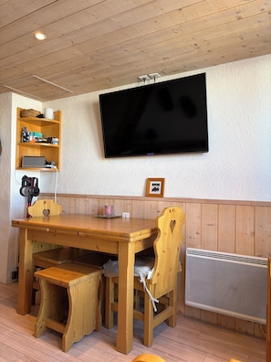 A wooden dining area with a TV mounted on the wall, a wooden table, and chairs.