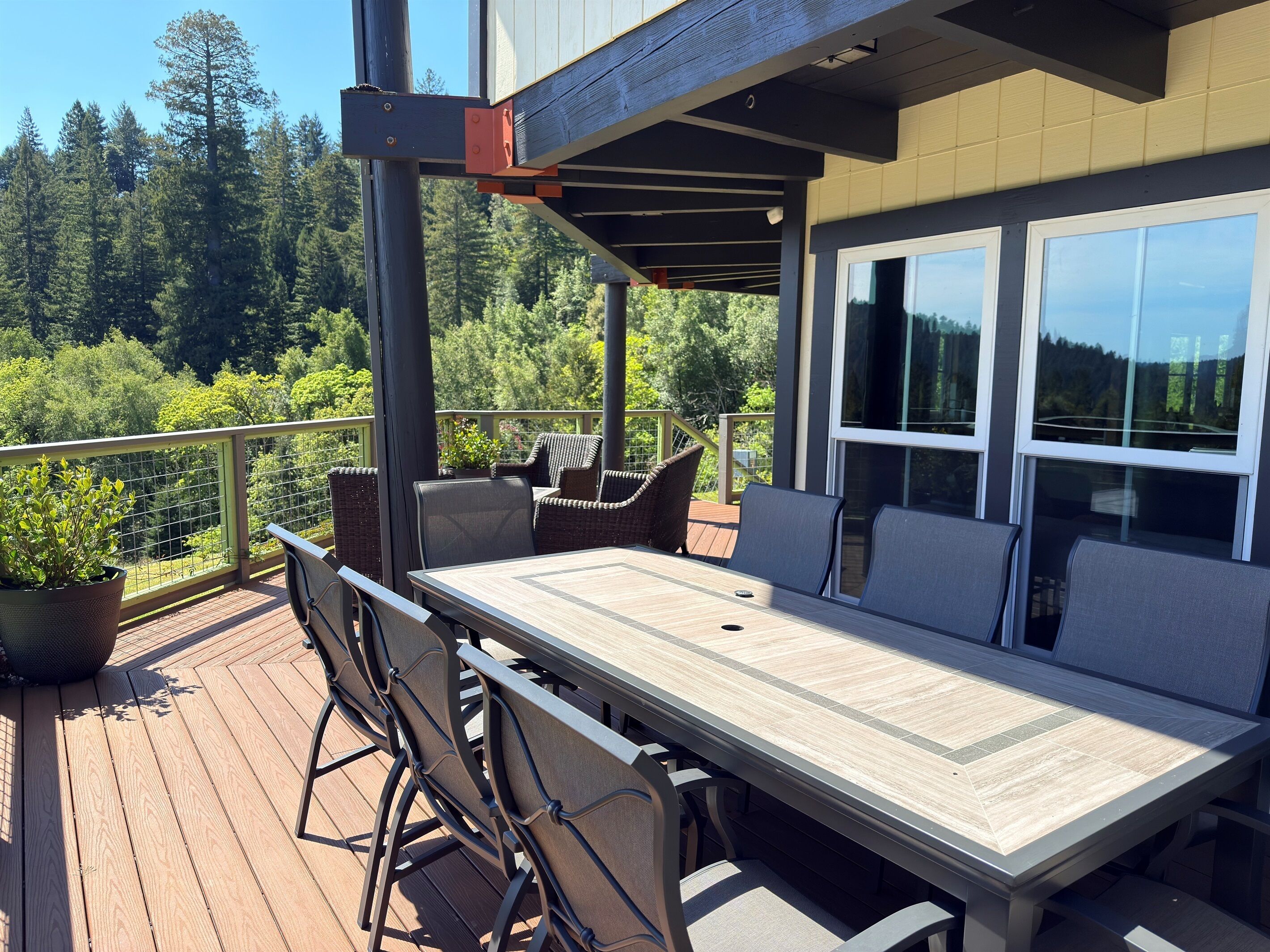 An outdoor deck with a dining table and chairs, surrounded by a wooden railing and potted plants.