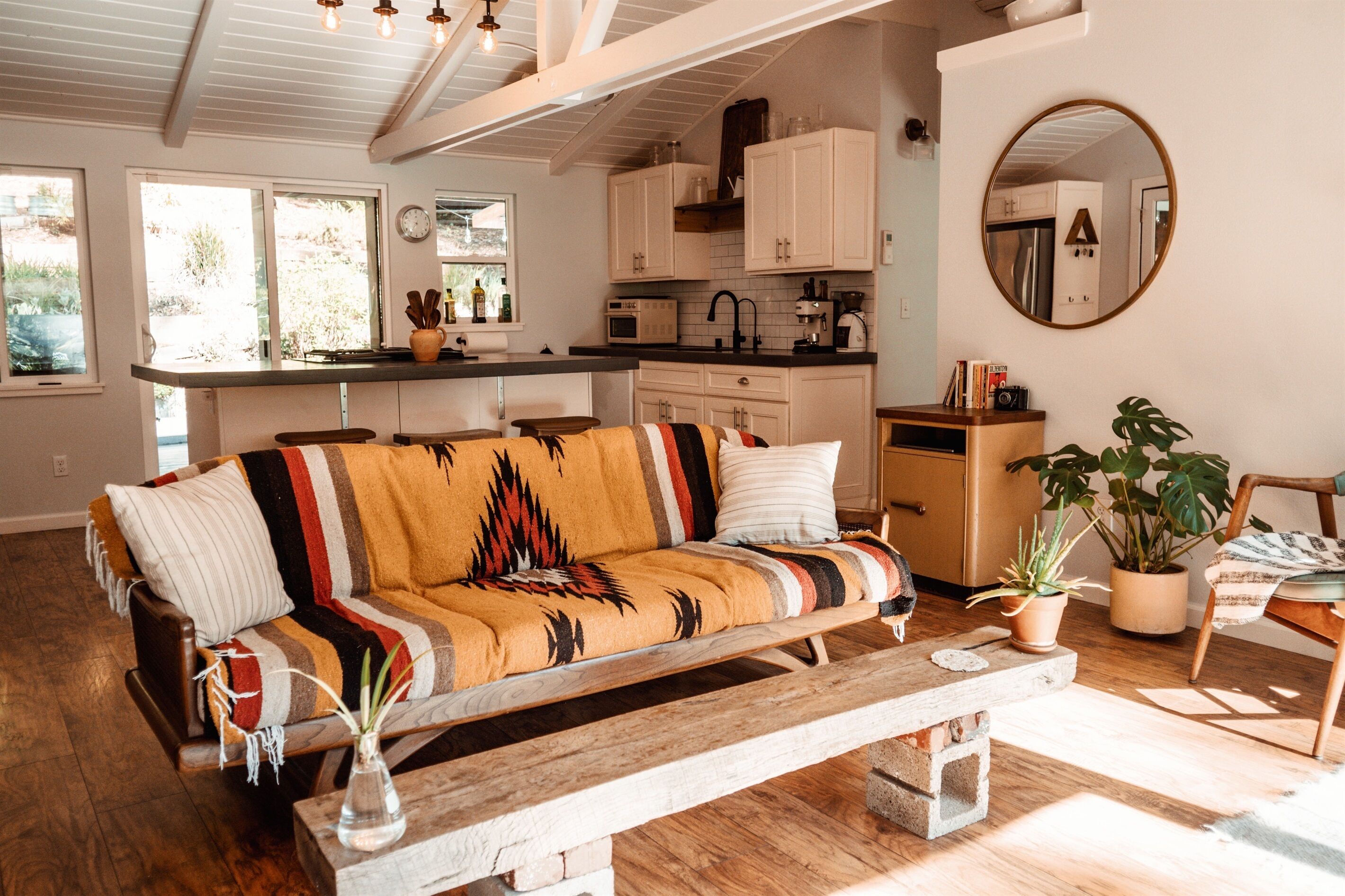 A cozy living room with a sofa, a wooden bench, and a coffee table. There is a kitchen area with cabinets and a countertop.
