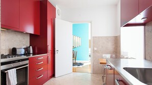 A modern kitchen with red cabinets, stainless steel appliances, and a view into a dining area. - Chiado Glamorous flat! FREE PARK! Great WI-FI!! (Lisboa)