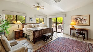 A bedroom with a bed, a desk, a chair, a bench, a lamp, and a large window. - On the Rocks - Beautiful 3 BR / 2 bath home nestled in the heart of West Sedona (Sedona)