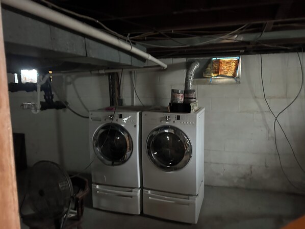A laundry room with two stacked front-loading washing machines, a ventilation duct, and a small window.