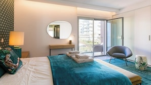 Et moderne hotelværelse med en stor seng, et siddeområde med en stol, et skrivebord med lampe og udsigt udad.