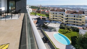 En balkon med udsigt over en swimmingpool, en parkeringsplads og en bygning med flere etager.
