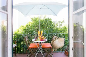 A balcony with a table set for a meal, a wicker bag, and a large umbrella. - Principe Real Orange tree w/ view 3 bedrooms flat! (Lisbon)