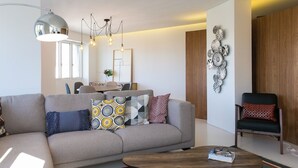 Ein modernes Wohnzimmer mit einem grauen Sofa, gemusterten Kissen, einem Holztisch und einem Essbereich im Hintergrund.